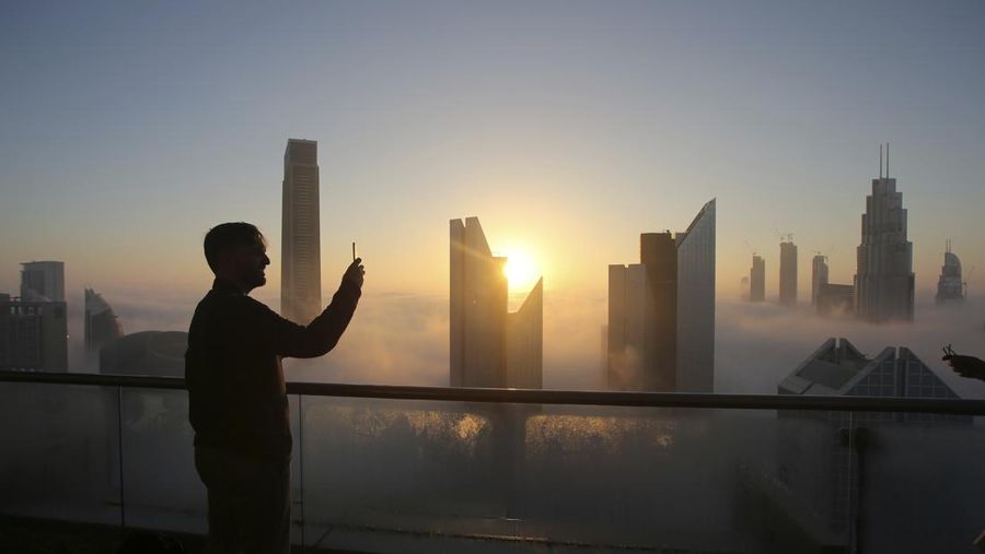 Seorang pria mengambil foto saat matahari terbit di atas cakrawala kota dari balkon di lantai 42 sebuah hotel pada hari berkabut di Dubai, Uni Emirat Arab. (AP Photo/Kamran Jebreili/File Foto)