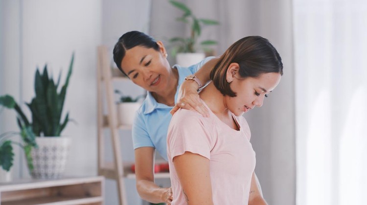 Asian woman, chiropractor and therapist with patient for back pain, relief or spine injury at clinic. Female person or young practitioner helping customer with backache or tension in physiotherapy
