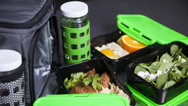 tupperware A set of black and green food storage Tupperware like containers with fresh salad, fruit, and meal prep food with an insulated travel bag.