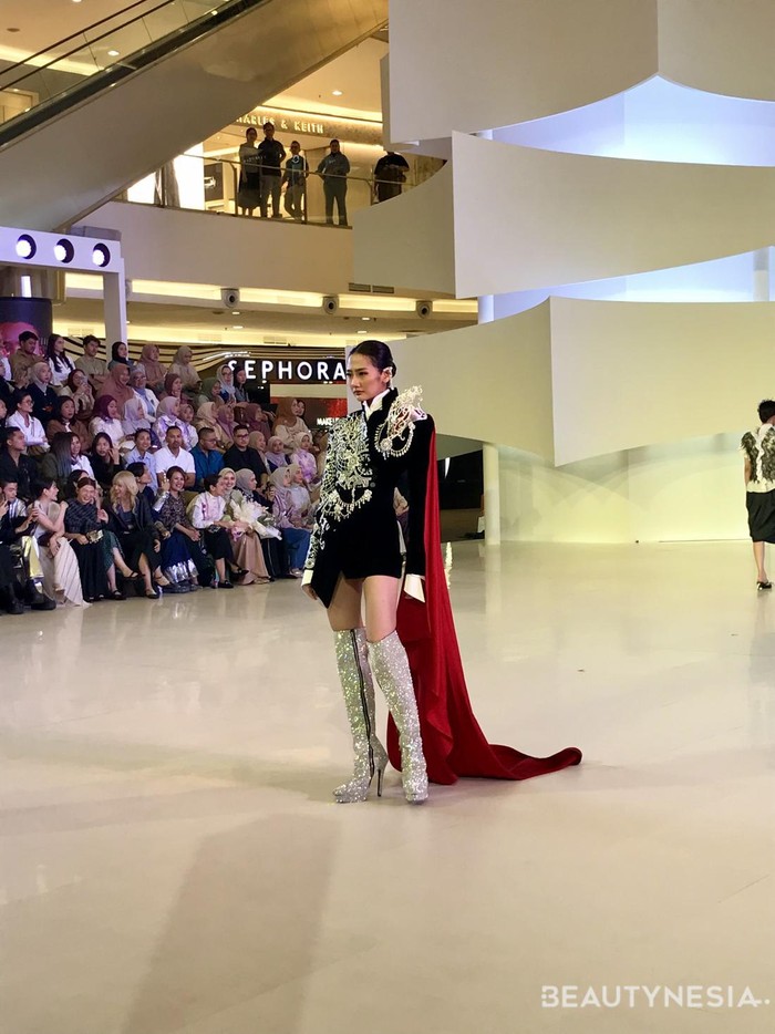 Danny Satriadi beri sentuhan cape merah pada busana hitam-putihnya. Sebuah micro mini dress memiliki siluet sedikit oversized, serta bordiran perak serta aksesori Rinaldy Yunardi membuat bold statement pada busana/ Foto: Dok. Beautynesia