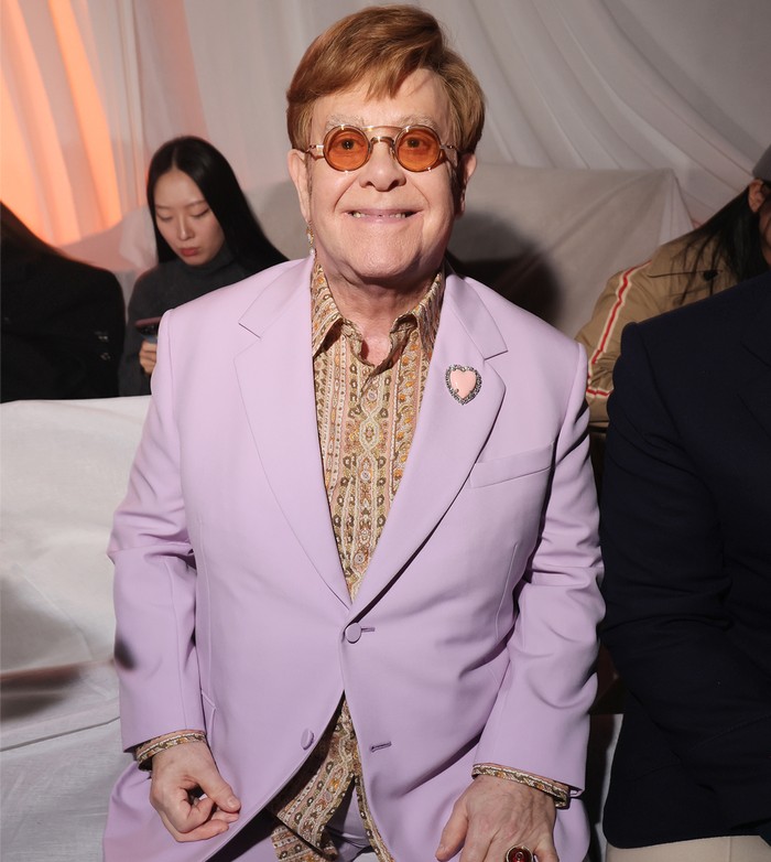 Sir Elton John turut dijumpai di jajaran bangku front row, Beauties. Tanpa meninggalkan gaya personalnya, penyanyi Rocket Man ini memadukan setelan jas lilac dengan kemeja bermotif. Bros bentuk hati disematkan di bagian lapels menegaskan impresi quirky/ Foto: Courtesy of Valentino