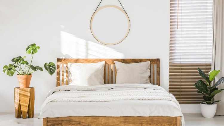 Sun shining on a white wall with a round mirror in a minimalist bedroom interior with natural, wooden furniture and beautiful green plants