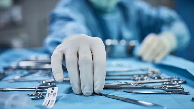Surgeon picking up surgical tool from tray. Surgeon is preparing for surgery in operating room. He is in a hospital.