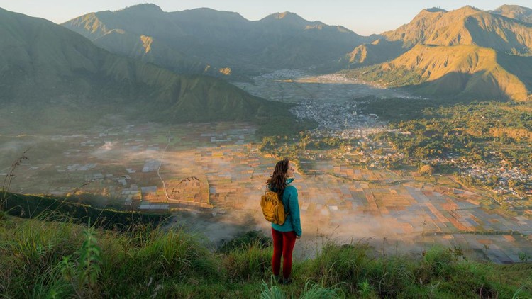 Woman  with backpack standing on viewpoint after hike near mount Rinjani on Lombok island