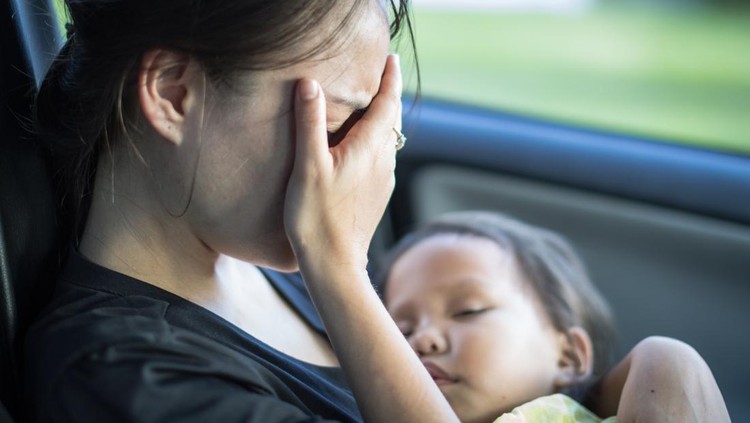 A parent covering her face, exhausted from taking care of her baby. Resting in the car.