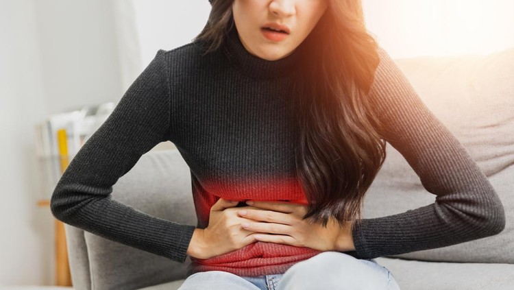 Young woman suffering from strong abdominal pain while sitting on sofa at home