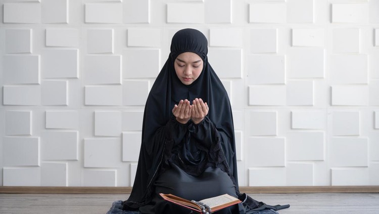 Muslim woman pray on hijab praying with Koran on mat indoors