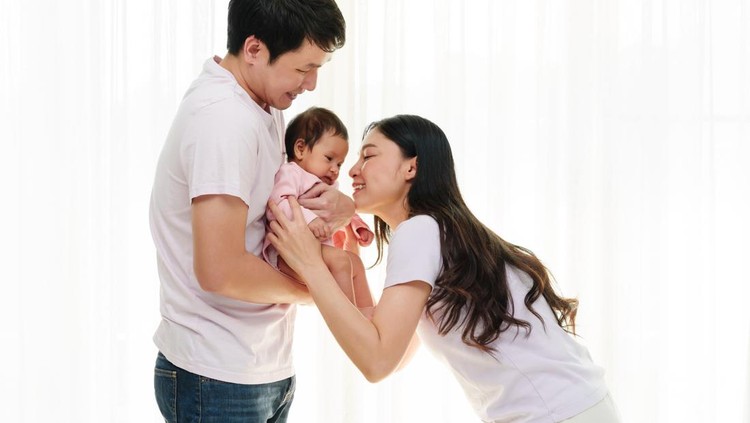 cheerful father and mother holding and playing with newborn baby on white window background. happy family concept
