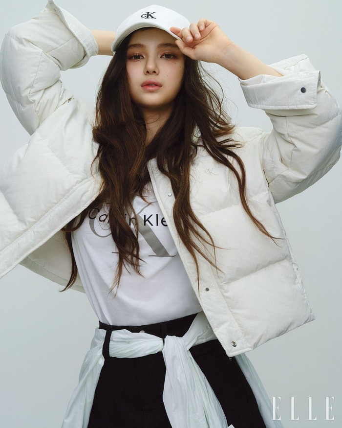 Danielle tampil chic dengan memakai jaket quilted putih dan T-shirt berlogo dengan desain crew neck. Ia melengkapinya dengan rok mini denim high-rise, kemeja yang melingkari pinggangnya, dan ball cap putih. / Foto: Elle Korea