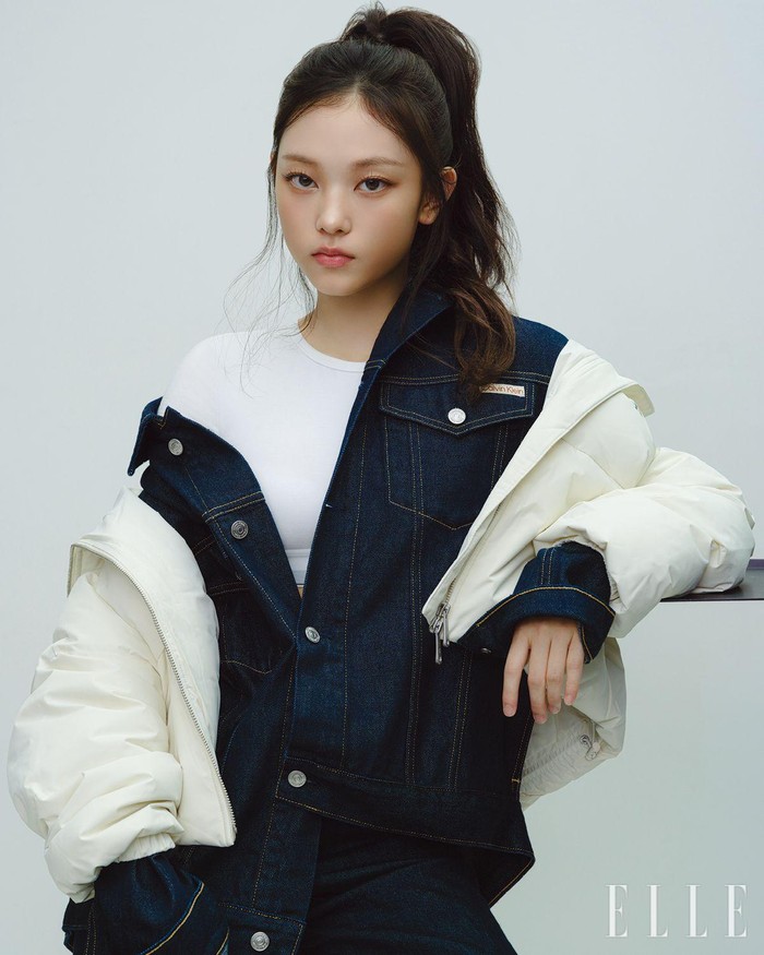 Haerin tampil memukau dengan gaya kasual yang tetap stylish dengan jaket puffer cropped down, jaket denim berbahan katun daur ulang, bralette T-shirt katun, dan celana denim wide leg. / Foto: Elle Korea