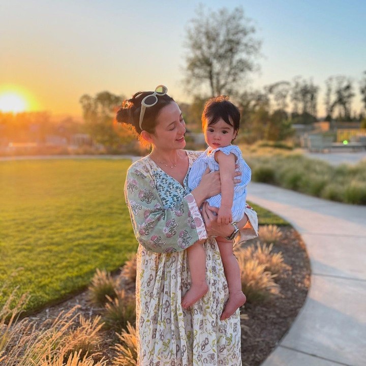 <p>Sambil menggendong sang putri, Brielle Leia Tjiptobiantoro, Julie terlihat sederhana dengan <em>dress</em> lengan panjang kombinasi warna kuning dan hijau. Ia juga mengenakan aksesori jam tangan dan kalung. (Foto: Instagram: @julstelle)</p>