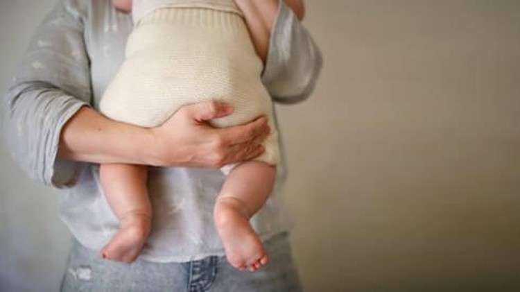 mother holds her baby in eco-friendly diaper&comma; conscious consumption and motherhood&comma; eco-friendly swaddling systems and replacement of disposable diapers&comma; faceless and close up