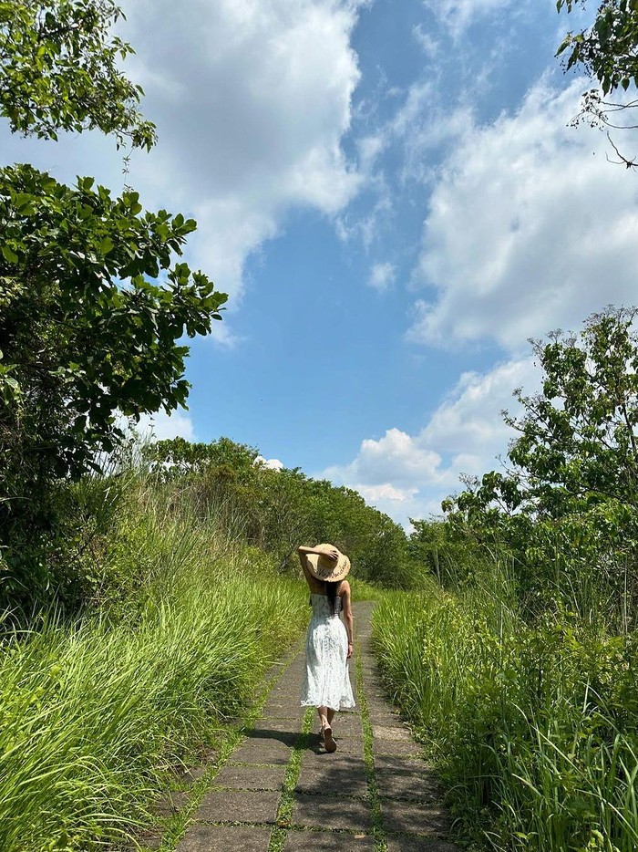 Tampil manis dalam balutan gaun putih dan topi pantai, Lee Mi Joo menyusuri jalanan setapak panjang yang menyimpan kesejukan luar biasa dengan pepohonan hijau di Bukit Campahan Ubud./ Foto: instagram.com/queen.chu_s