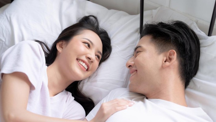 Happy Asian couple lying down smiling and relaxing together in bed.