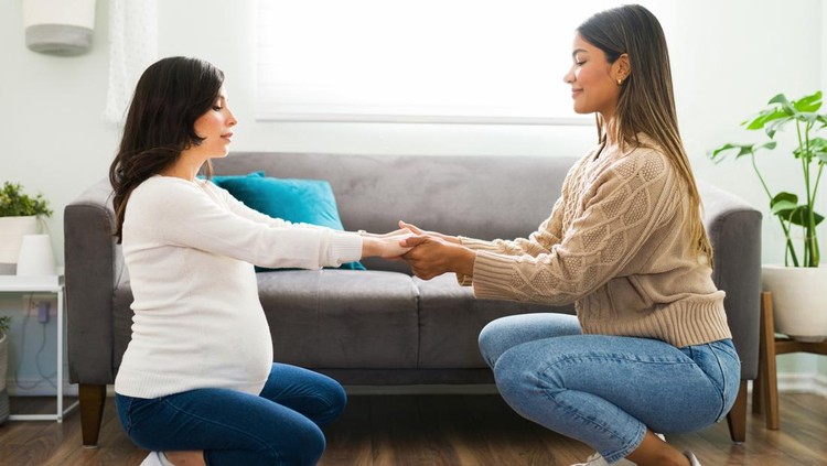 Smiling midwife helping a beautiful pregnant woman with her stretching exercises. Happy doula giving support to an expectant mother to induce labor