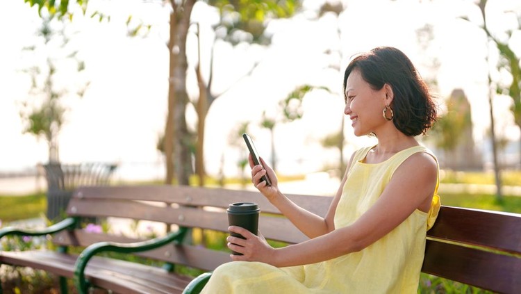 Ilustrasi perempuan dengan outfit sesuai personal color Portrait of a young Asian woman using a smartphone while enjoying a cup of coffee in the park, savoring a beautiful day outdoors and breathing in the fresh air.