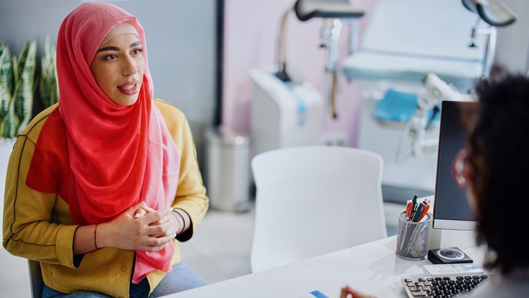 A Muslim woman sits across from her female doctor as she talks with her about cervical cancer