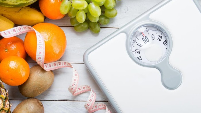 Stack of fruits, white weight scale and tailor meter on wooden board. Concept of diet and healthy lifestyle