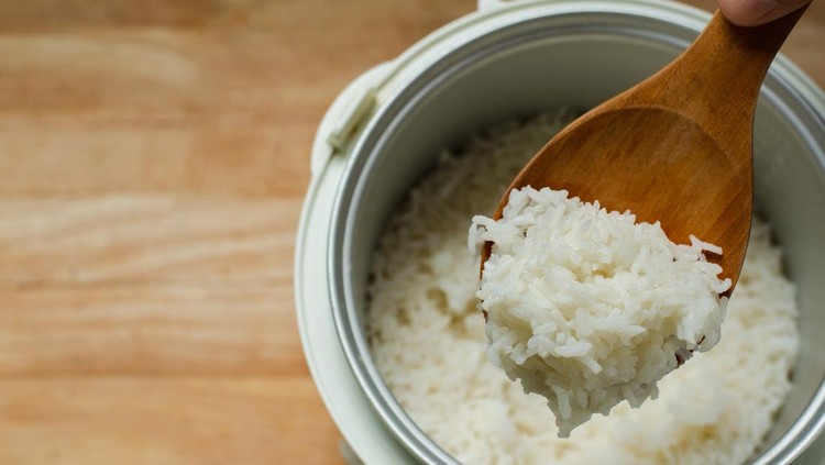 Jasmine rice cooking in electric rice cooker with steam, Hand hold wooden ladle in electric rice cooker in the kitchen.