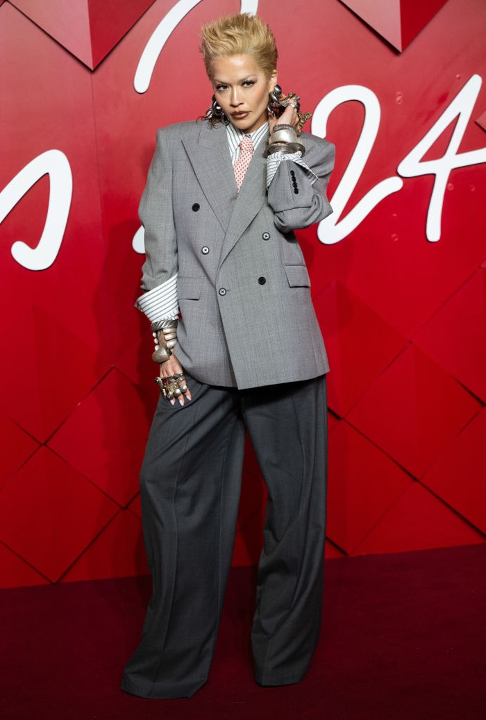 Rita Ora pancarkan pesona androgini yang eksentrik lewat balutan setelan jas dari Primark berpotongan longgar, lengkap dengan kemeja bergaris dari dasi. Kedua lengan double-breasted jacket sengaja ditekuk untuk memperlihatkan permainan aksesori yang edgy nan dramatis./ Foto: WireImage/Samir Hussein
