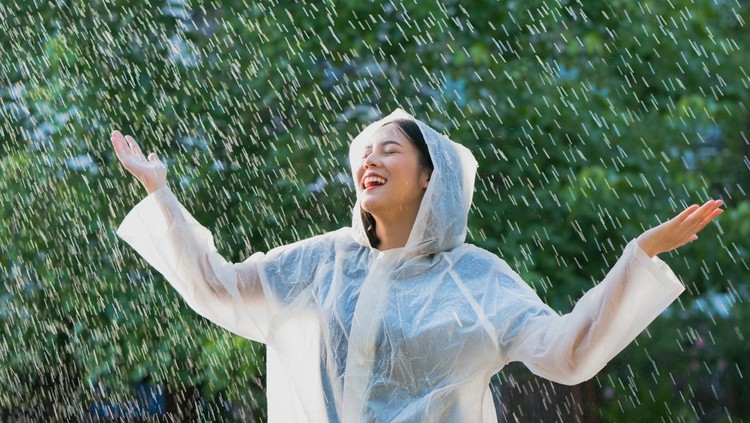 Rainy day asian woman wearing a raincoat outdoors. She is happy.