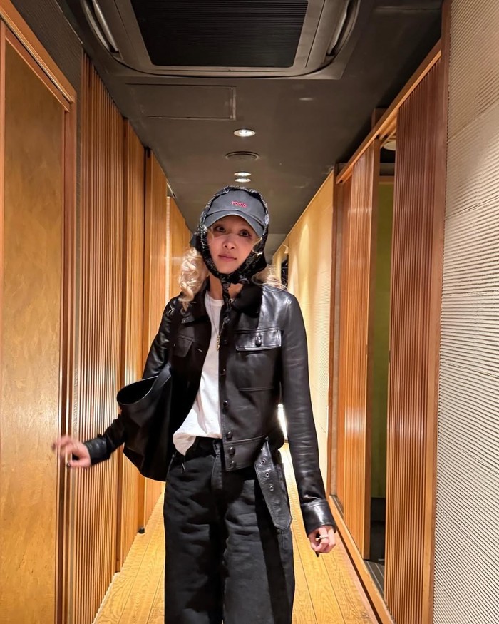 Jaket kulit Rosé menjadi pusat perhatian kali ini. Dipadukan dengan kaus putih simpel, celana dan tas hitam besar menambah kesan nyaman. Aksesori topi dan scarf memberi sentuhan unik dan stylish pada keseluruhan look./ Instagram/roses_are_rosie