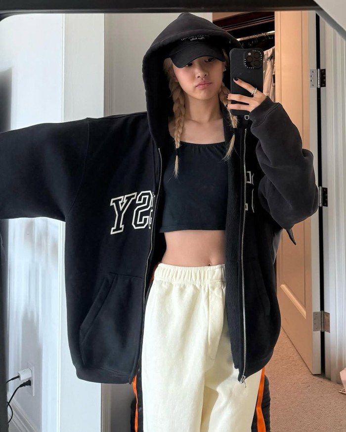 Outfit Rosé ini memadukan gaya kasual yang trendi. Ia memadukan jaket hitam oversized dengan crop top hitam minimalis, celana jogger putih, serta topi hitam untuk melengkapi look streetwear yang effortless namun stylish./ Foto: Instagram/roses_are_rosie