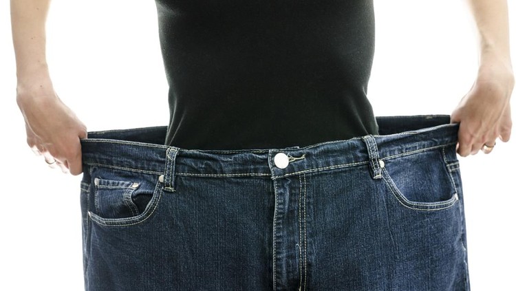 Woman showing how much weight she lost by wearing her old jeans. Weightloss concept.