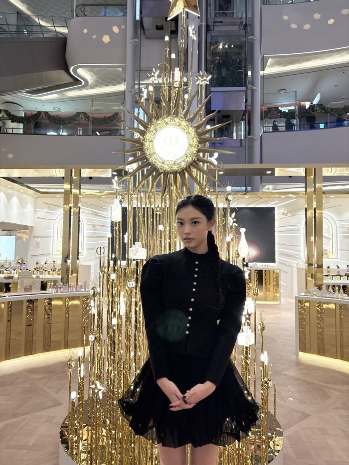 Tampil elegan dalam balutan busana serba hitam, idol K-Pop yang sudah genap berusia 18 tahun tersebut kembali menjadi sorotan publik. Ia terlihat mencolok di antara dekorasi yang bersinar keemasan di sekelilingnya./ Foto: x.com/NewJeans_ADOR