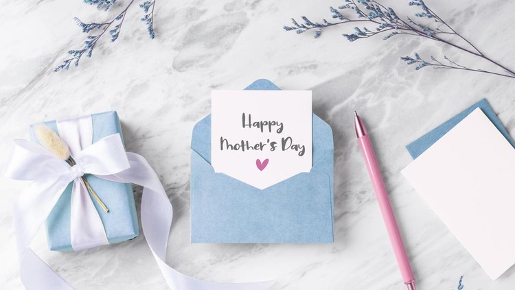 Mother's day card with blue gift box and envelope on marble table with flower and pen, top view