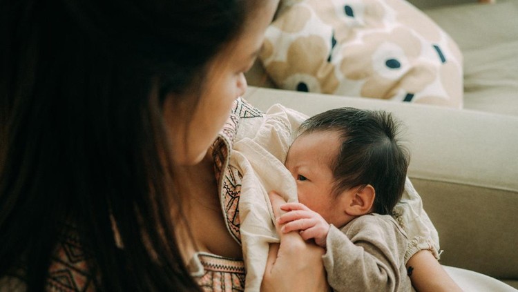 A mother sits in an armchair&comma; holding her newborn in her arms&comma; gazing lovingly at her baby&period;