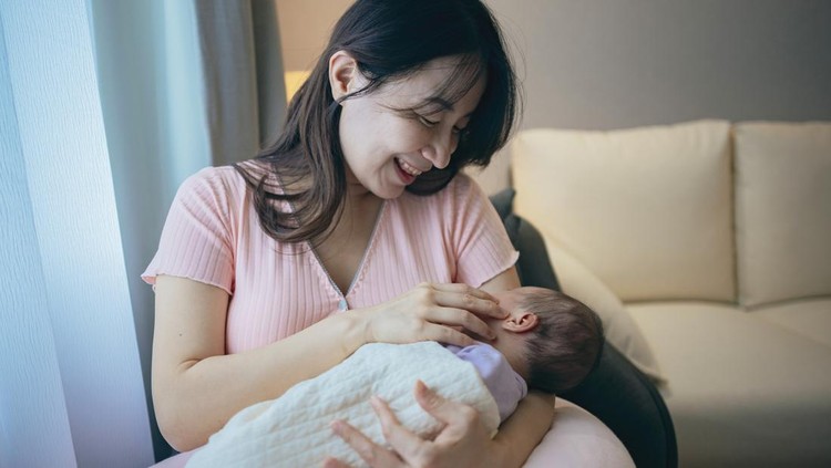 Ilustrasi menyusui A mother sits in an armchair, holding her newborn in her arms, gazing lovingly at her baby.