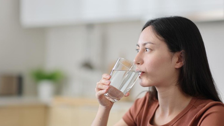 Asian woman drinking tap water from glass in the kitchen