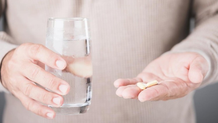 Pria minum obat A man holding a glass of cold water and a pill, illustrating the common misconception of taking medication with cold water. Highlights the potential risks and importance of proper medication practices
