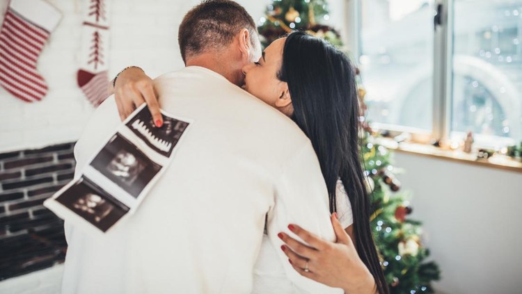 USG hamil Happy pregnant woman with baby ultrasound photo embracing with her husband infront of the Christmas tree