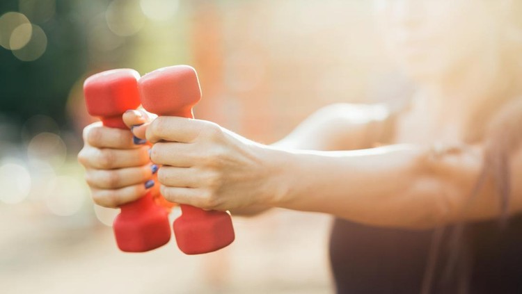 Girl making exercises with dumb-bells in the park. Shalow depth of field.