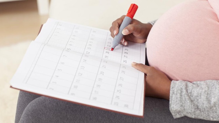 Baby due date - unrecognizable pregnant woman wi big belly in pink t-shirt marking off dates on calendar, using red marker.
