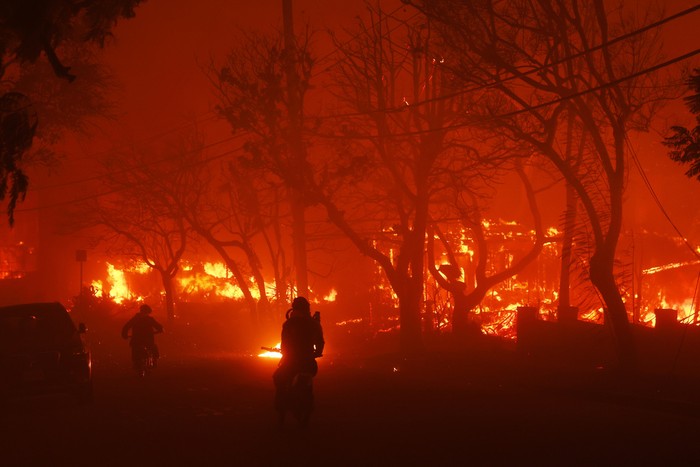 Two persons ride by on motorcycles as the Palisades Fire destroys a neigbhborhood in the Pacific Palisades neighborhood of Los Angeles, Tuesday, Jan. 7, 2025. (AP Photo/Etienne Laurent)