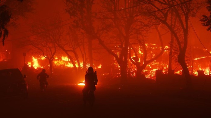 Two persons ride by on motorcycles as the Palisades Fire destroys a neigbhborhood in the Pacific Palisades neighborhood of Los Angeles, Tuesday, Jan. 7, 2025. (AP Photo/Etienne Laurent)