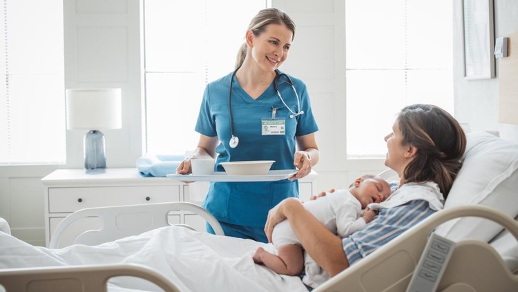 Nurse bringing food for mother at hospital bed. Mother is holding newborn baby.