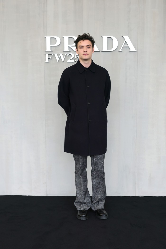 Louis Partridge terlihat simpel dan elegan mengenakan coat hitam yang dipadu padan dengan loose pants motif herringbone/ Foto: Dok. Prada