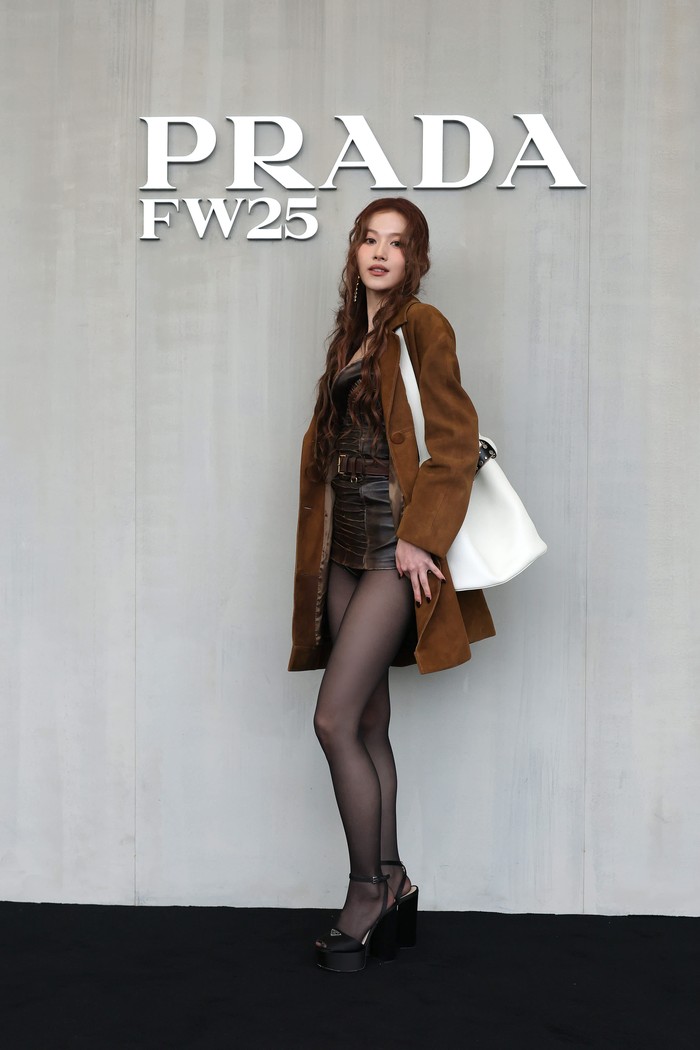 Tak kalah stylish dengan para pria, Sana TWICE menampilkan permainan tekstur dengan cara memadukan coat suede dengan mini dress leather. Penyanyi berdarah Jepang itu menyempurnakan look dengan stoking, Prada platform heels dan buckle bag nan edgy/ Foto: Dok. Prada