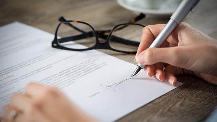 Closeup shot of a woman signing a form. She's writing on a financial contract. Shallow depth of field with focus on tip of the pen.