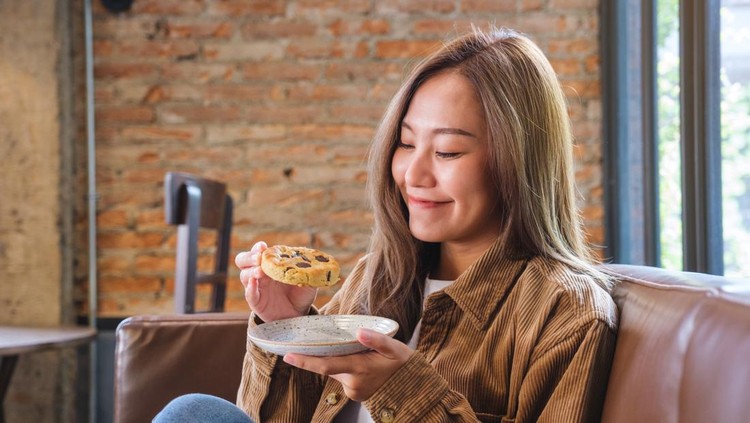 Portrait image of a beautiful young asian woman holding and eating cookie