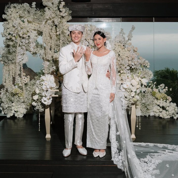 <p>Melalui foto-foto yang dibagikan di Instagram, Angga dan Shenina tampil serasi mengenakan pakaian bernuansa warna putih. Pakaian yang dikenakan Angga tampak seperti pakaian adat bernuansa Melayu. Sementara itu, Shenina terlihat cantik mengenakan kebaya <em>dress</em> putih dengan hiasan payet dan <em>veil</em> panjang yang dikenakan sebagai aksesoris di kepala. (Foto: Instagram @angga/ @sheninacinnamon)</p>