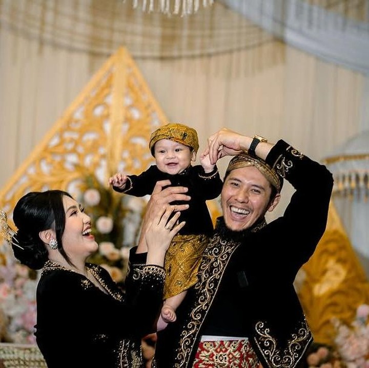 <p>Selama acara, Agham terlihat sangat anteng. Ia juga selalu menebarkan senyum ketika digendong oleh kedua orang tuanya. (Foto: Instagram: @viavallen)</p>