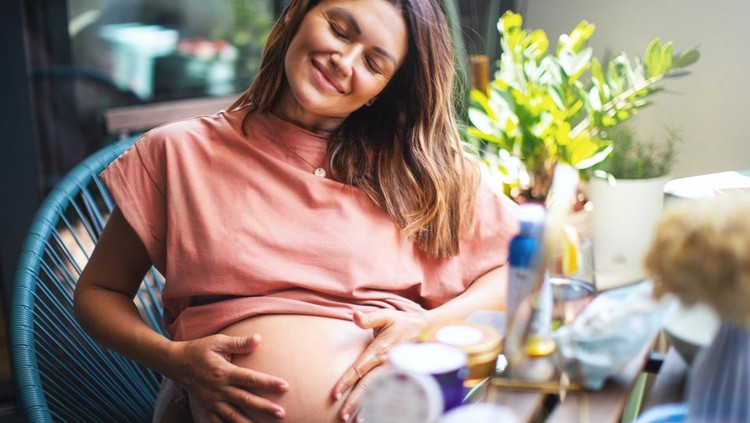 skincare ibu hamil Pregnant Woman Pampering Herself on the Terrace. Her Eyes are Closed and she's Smiling and Applying the Moisturizer on her Belly and taking care of her Skin during Pregnancy.