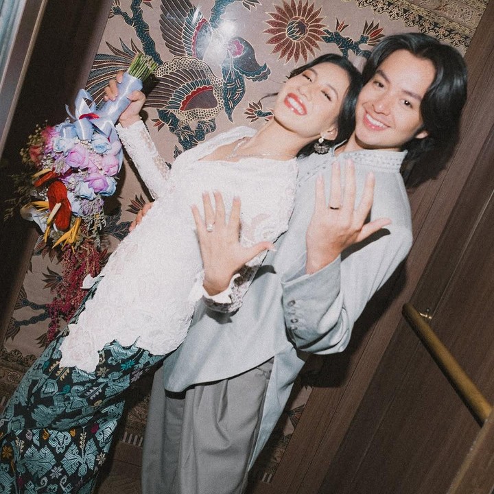 <p>Dalam satu foto, Shenina dan Angga memamerkan cincin pertunangan mereka. Acara lamaran semakin romantis lantaran suasana di ruangan dipenuhi dengan bunga warna-warni. (Foto: Instagram @angga/ @sheninacinnamon)</p>
