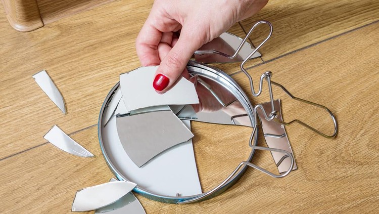 Woman's hand removes broken pieces of mirror from wooden floor at home