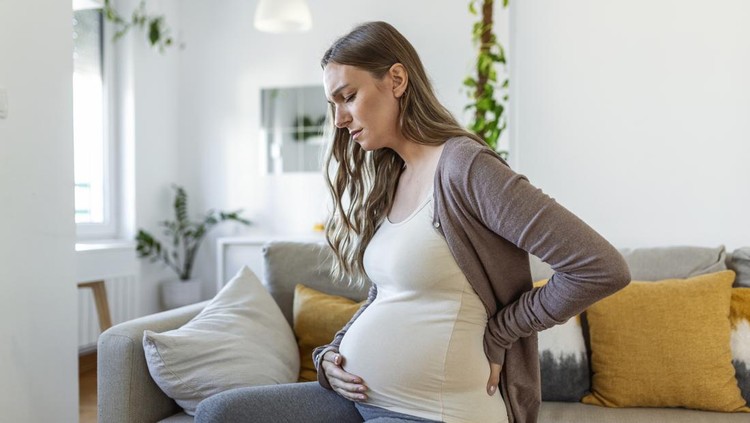 Tired stressed pregnant woman sitting on a couch and holding her belly